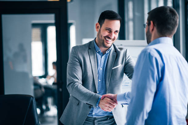 Two smiling businessmen shaking hands while standing in an office. - biotimes